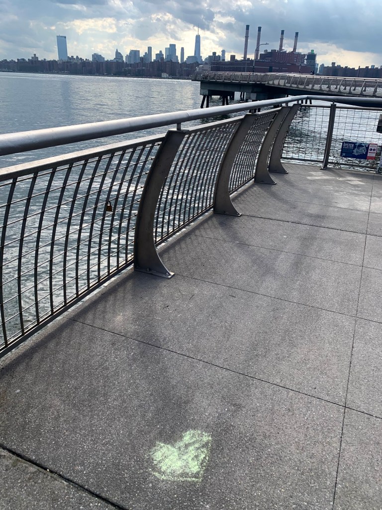 View of a waterfront area with a railing and a faint heart shape drawn on the pavement.