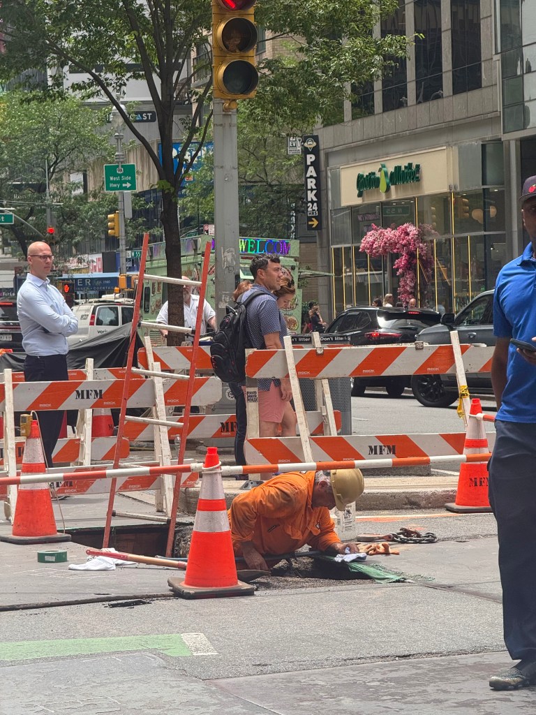 Construction worker in orange uniform working near a traffic light and road barricades in a city street.