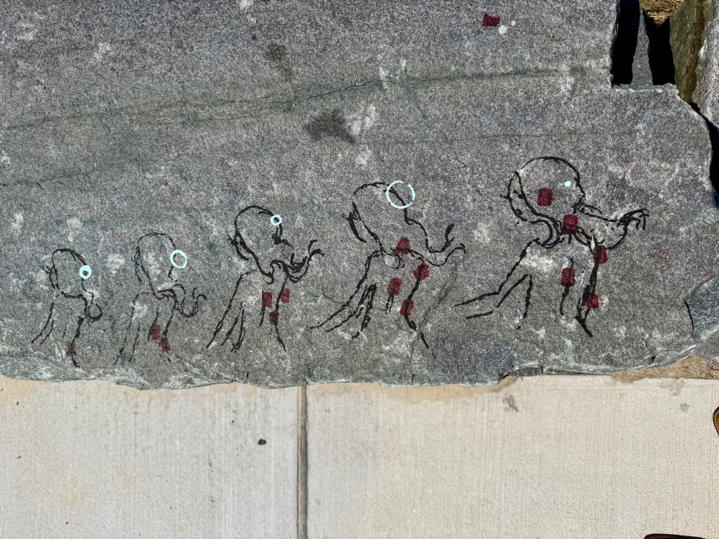 Ancient rock art depicting a sequence of figures resembling octopuses, with red and blue markings on a gray stone surface.