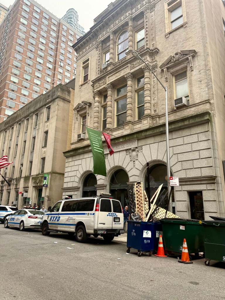 Street view of an ornate historic building with banners, parked police vehicles, and construction debris in front.