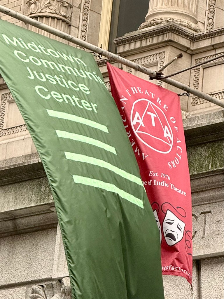 Two banners hanging outside a historic building: a green banner for Midtown Community Justice Center and a red banner for the American Theatre of Actors featuring a theatrical mask.