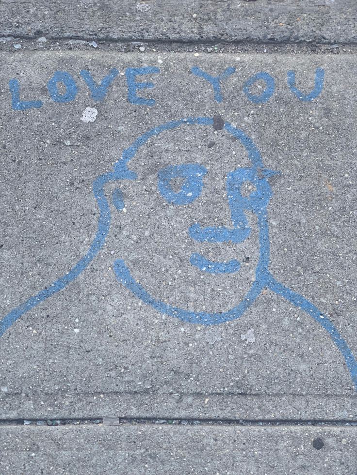 A sidewalk drawing featuring a smiling face with blue outlines and the words 'LOVE YOU' above it.