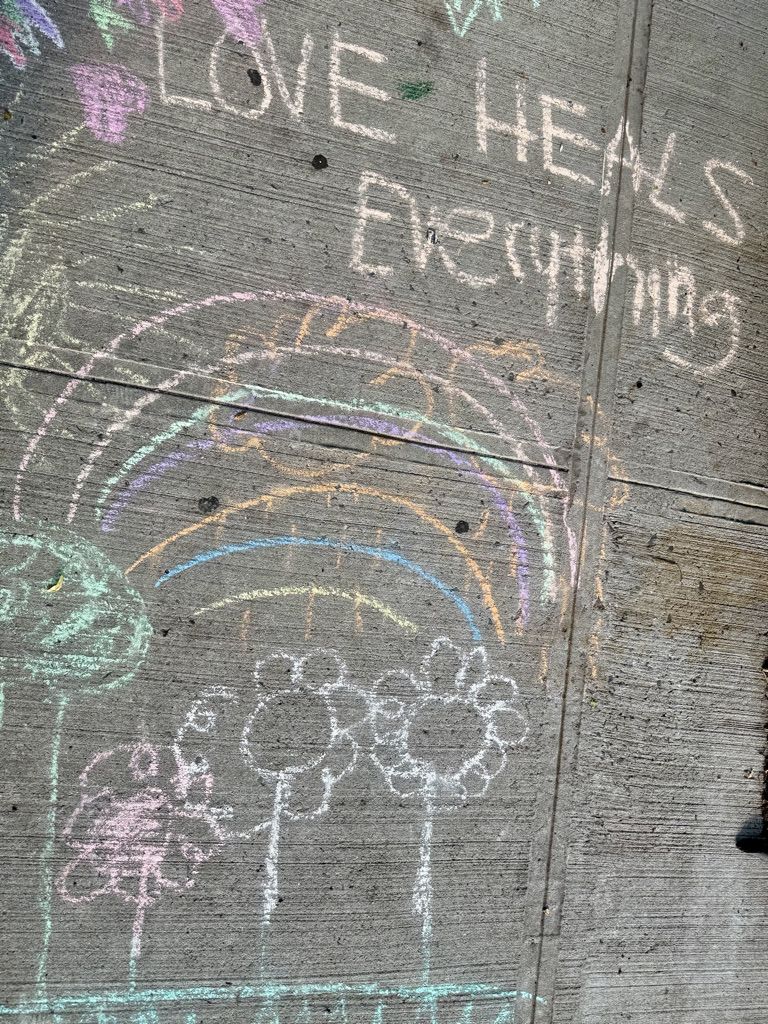Colorful chalk drawing on pavement featuring a rainbow, flowers, and the phrase 'Love Heals Everything.'
