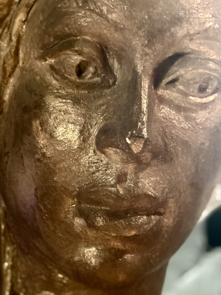Close-up of a sculpted face with a metallic finish, featuring distinct eyes and facial details.