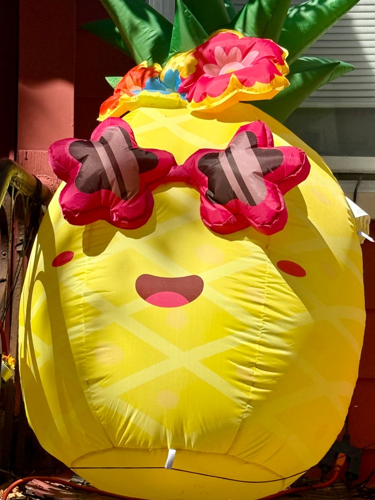 A large, inflatable pineapple decoration with sunglasses and floral accents, displaying a happy facial expression.