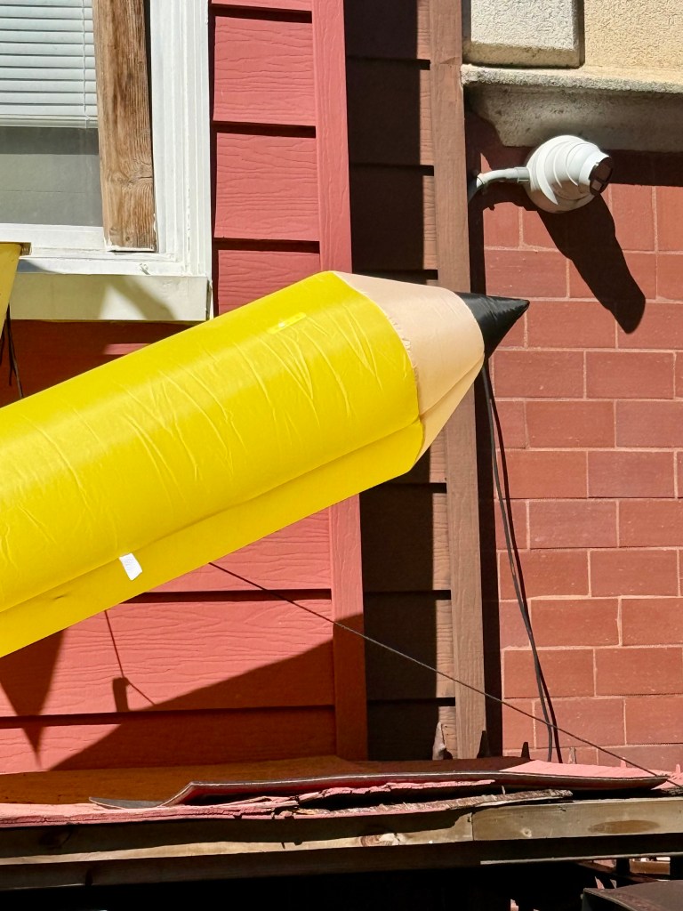 Large yellow inflatable pencil mounted on a wall beside a window.