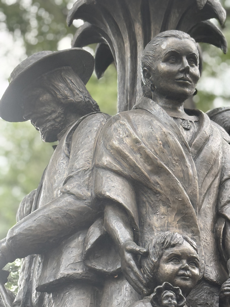 A close-up view of a bronze statue depicting two adults and a child, featuring a woman in traditional attire and a man with a hat, symbolizing family and heritage.