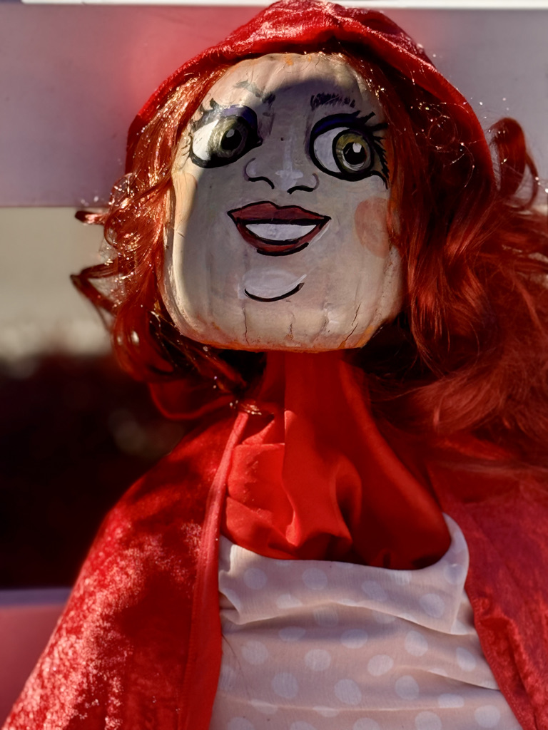 A doll with a painted face and vibrant red hair, wearing a red cloak and a polka-dot dress.