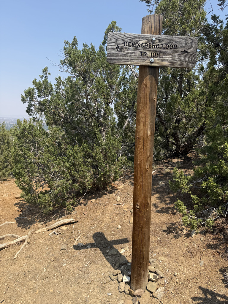 A wooden trail sign marking the Devisadero Loop with the trail number 108, surrounded by trees and rocky ground.