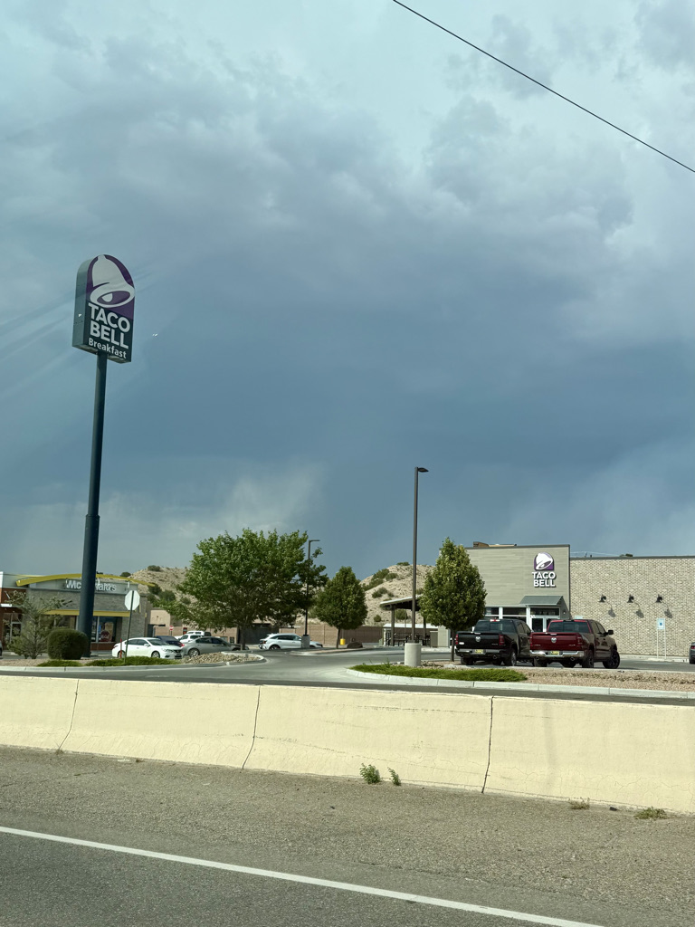 Taco Bell restaurant sign in front of a building under a cloudy sky, with additional fast food locations visible in the background.