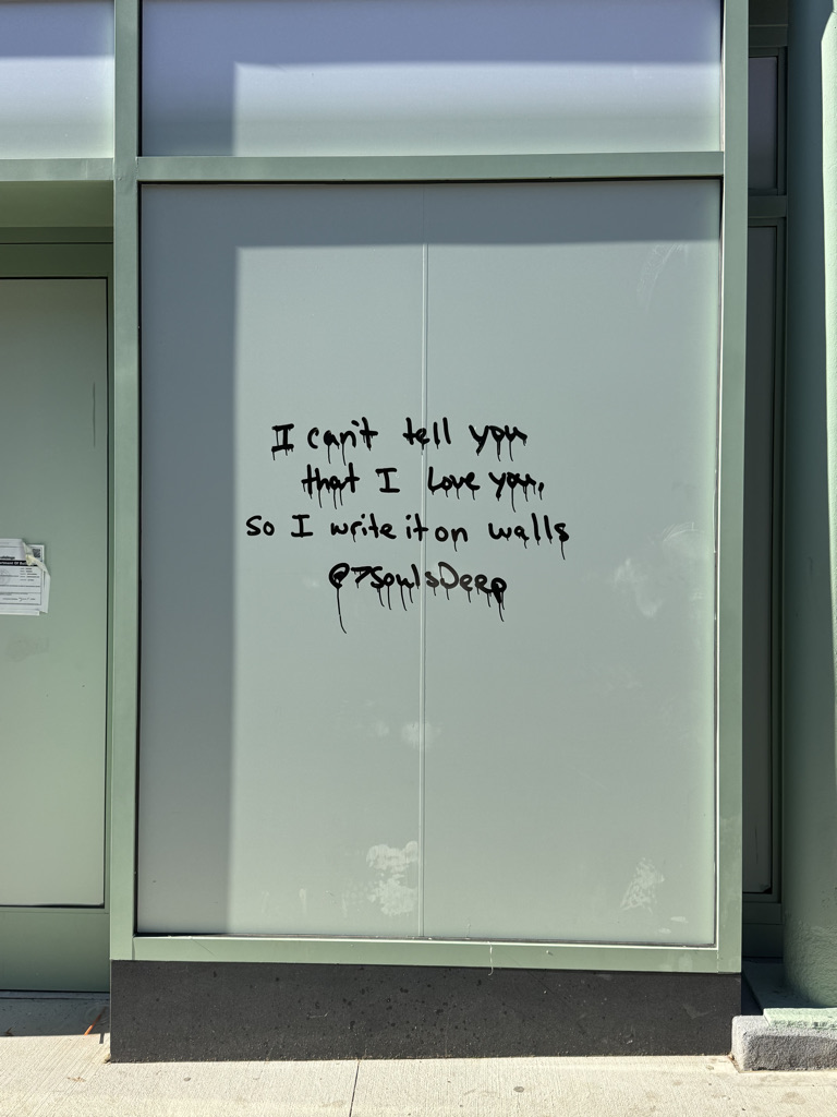 Graffiti on a wall displaying the text: 'I can't tell you that I love you, so I write it on walls' followed by a username '@Soul'sDeep'