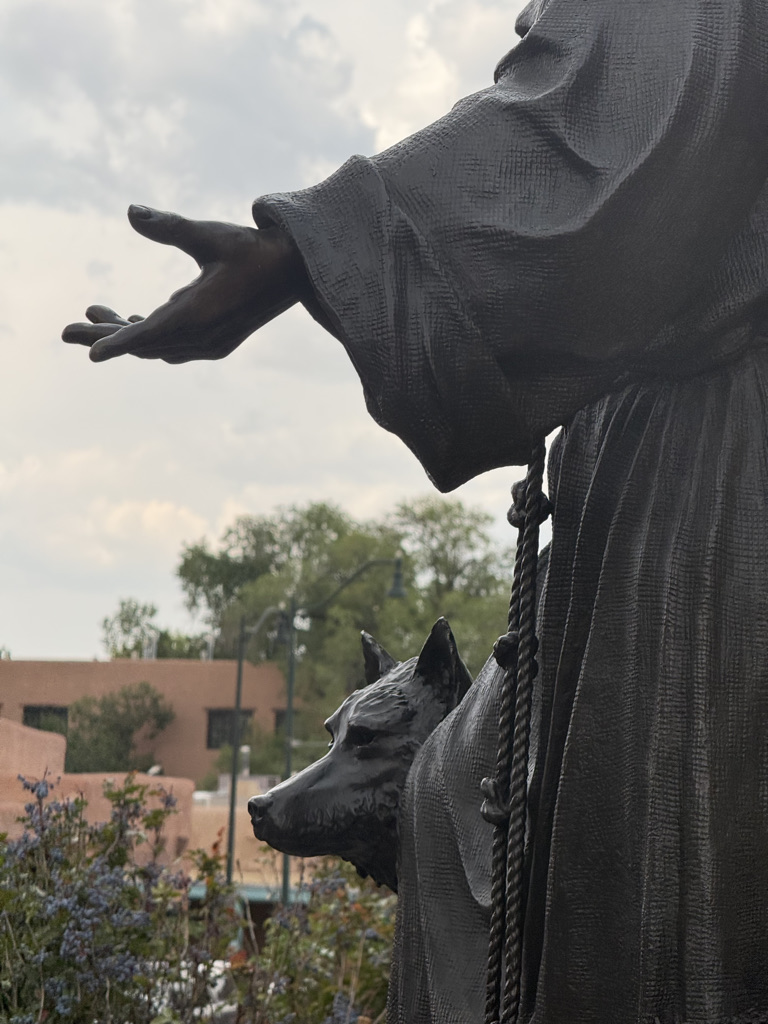 A close-up view of a statue depicting a figure with an outstretched hand, accompanied by a dog sculpture at its side, set against a cloudy sky.