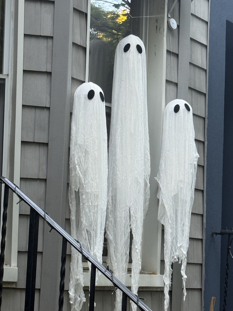 Three white ghost decorations with black eye patches hanging from a window.