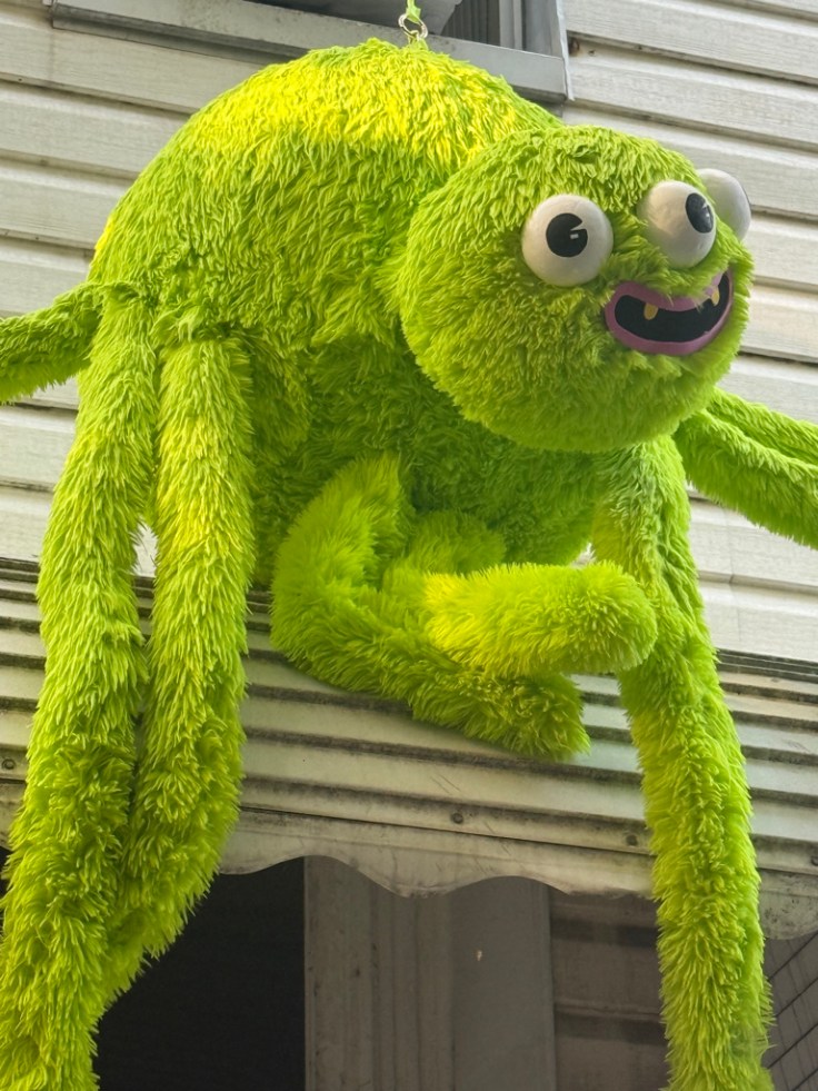 A large, bright green, furry creature resembling a friendly monster with multiple limbs and big googly eyes, perched on a window ledge.